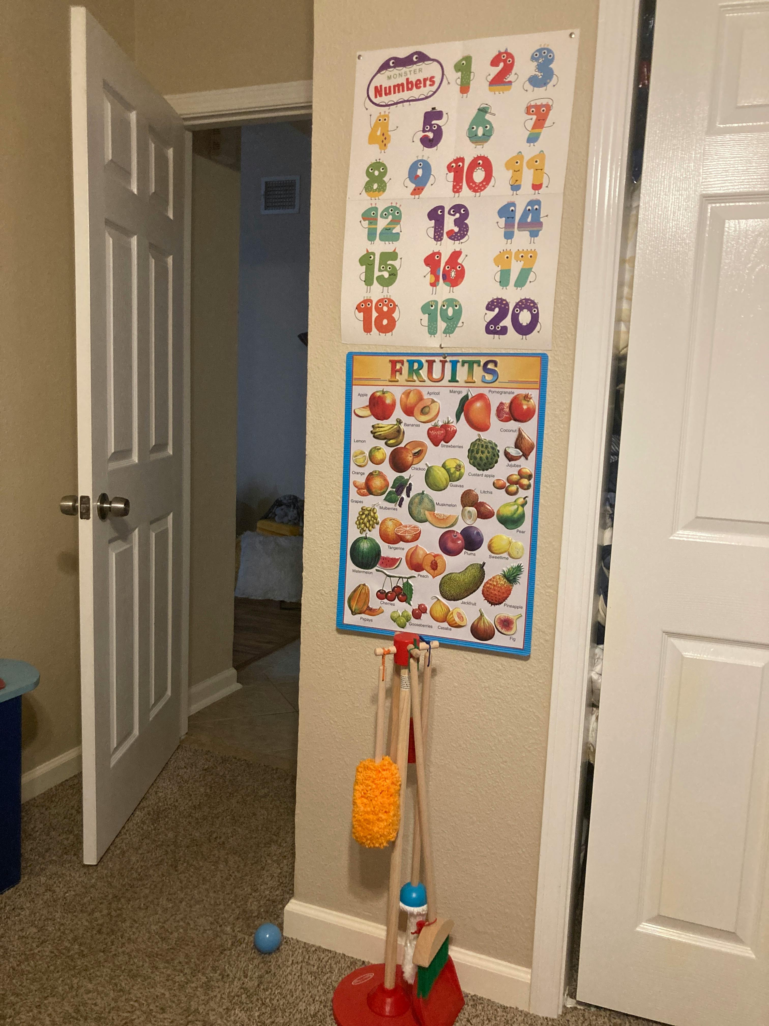 Numbers and fruits charts on a wall with a toy cleaning set
