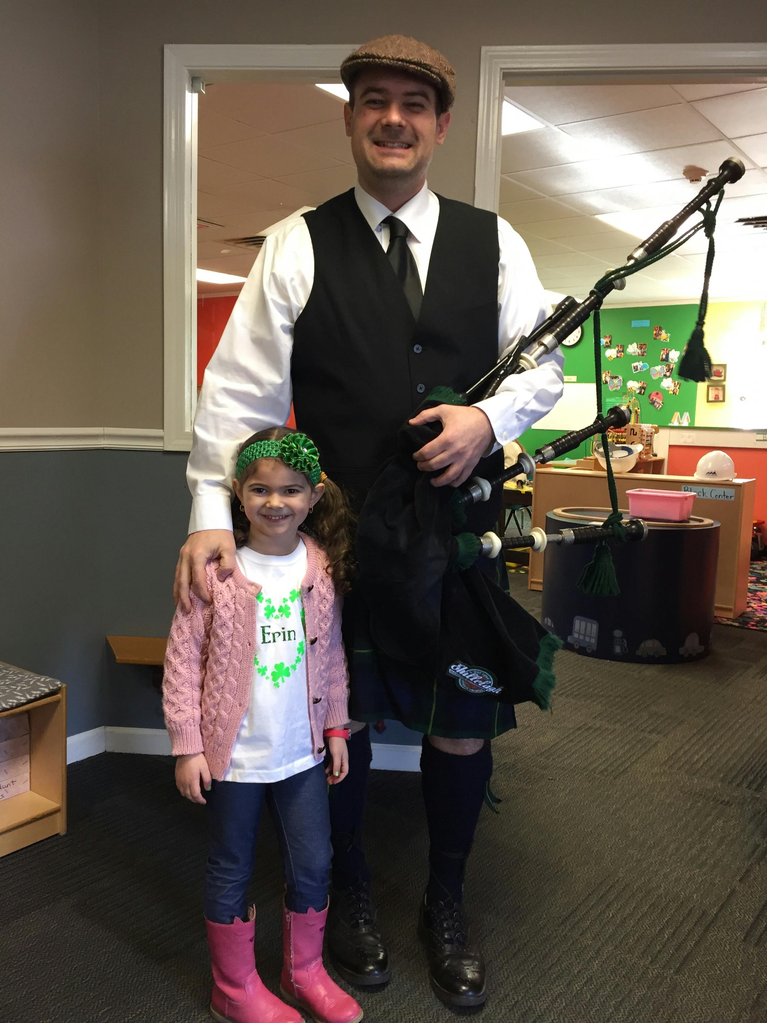 Person in kilt holding bagpipes with a child wearing a shirt that says Erin