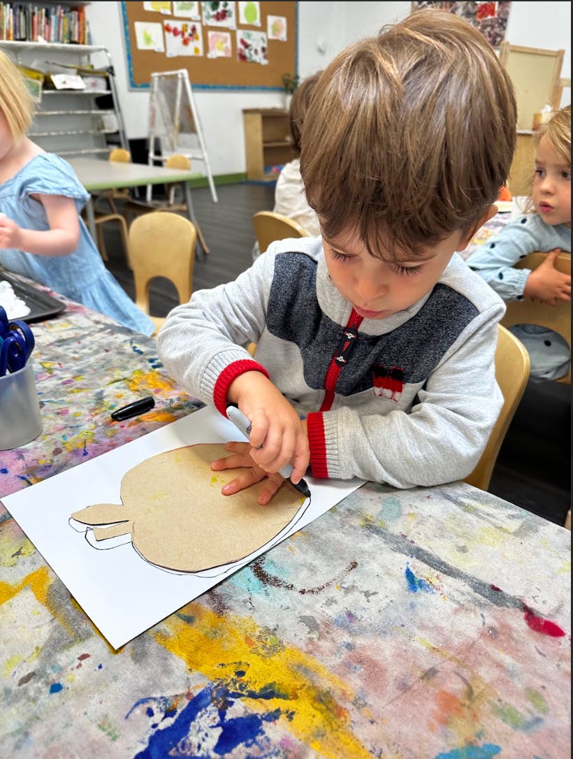 Child tracing an apple shape onto paper in a classroom