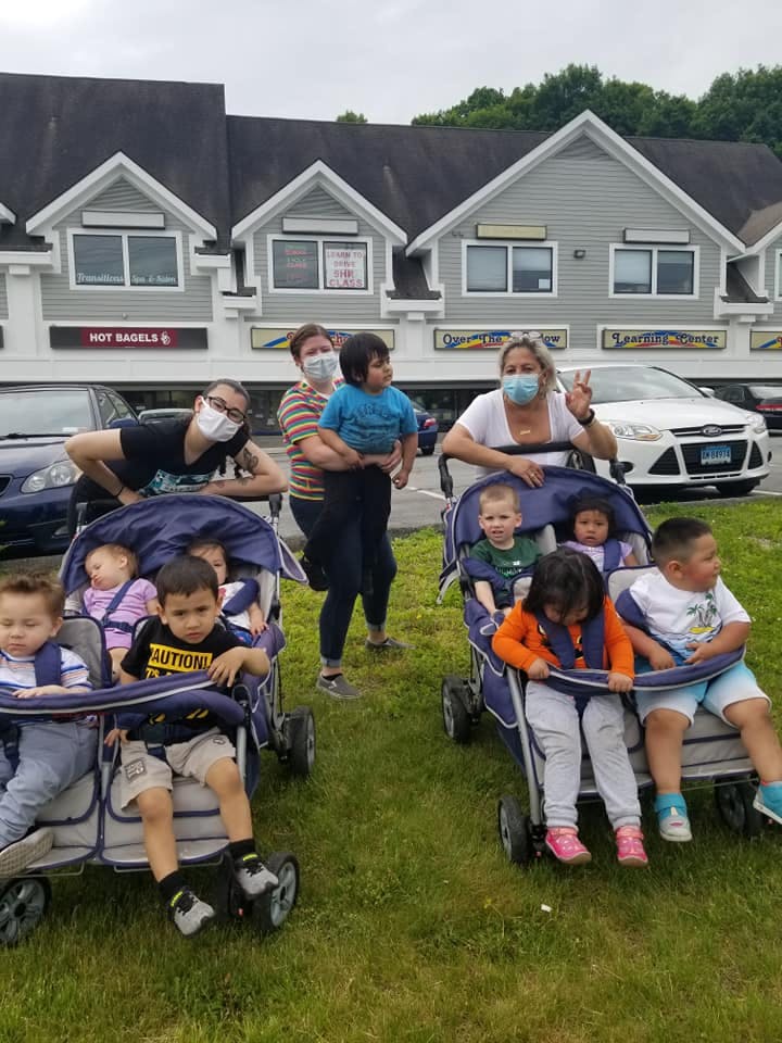 Adults and children in strollers on grass in front of buildings