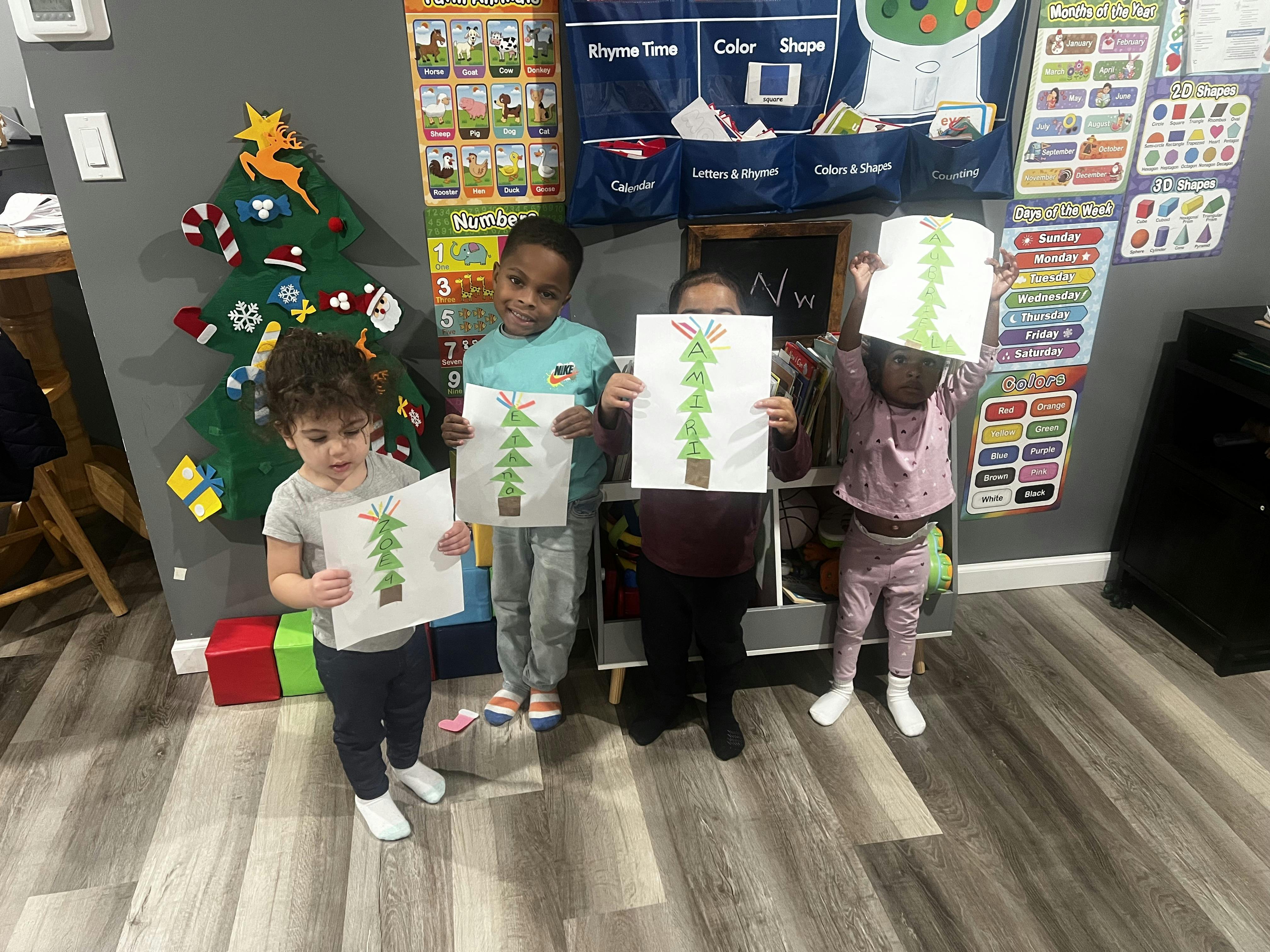 Four children holding up paper Christmas tree crafts with names on them