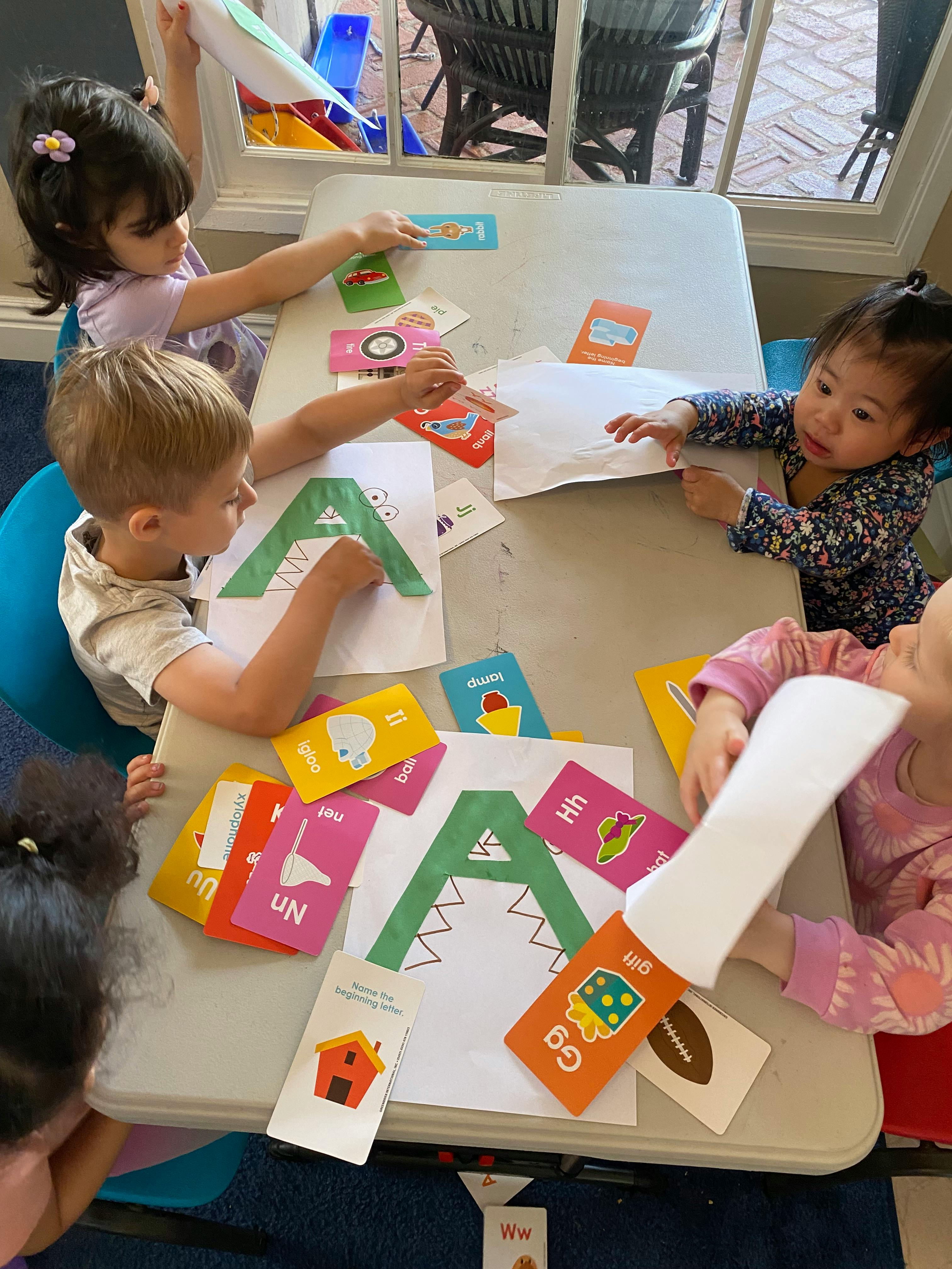 Children playing with alphabet cards and paper cutouts at a table