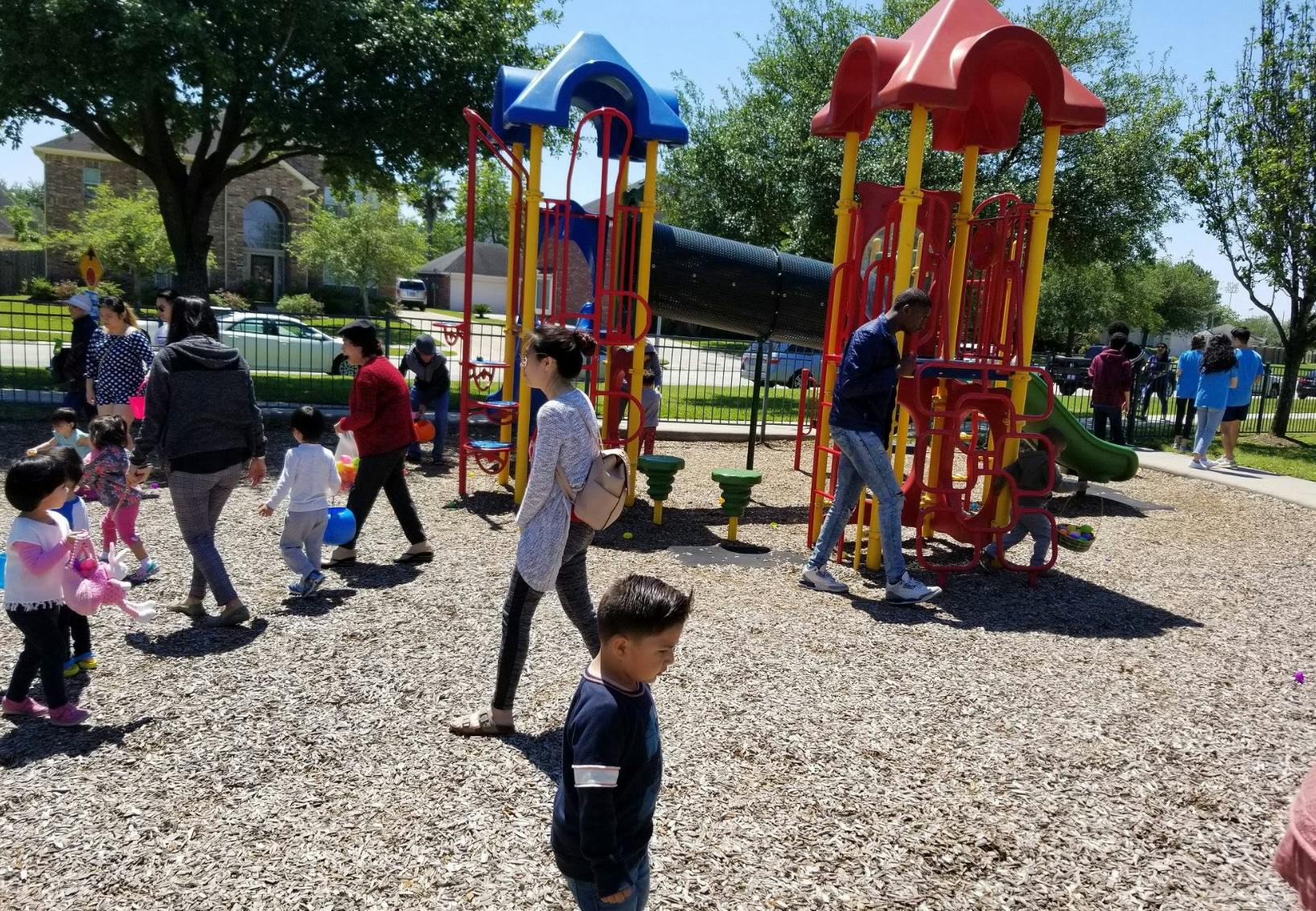 People and children on a playground with play structures