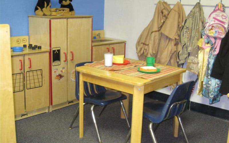 Child-sized table and chairs with play food next to a play kitchen in a classroom