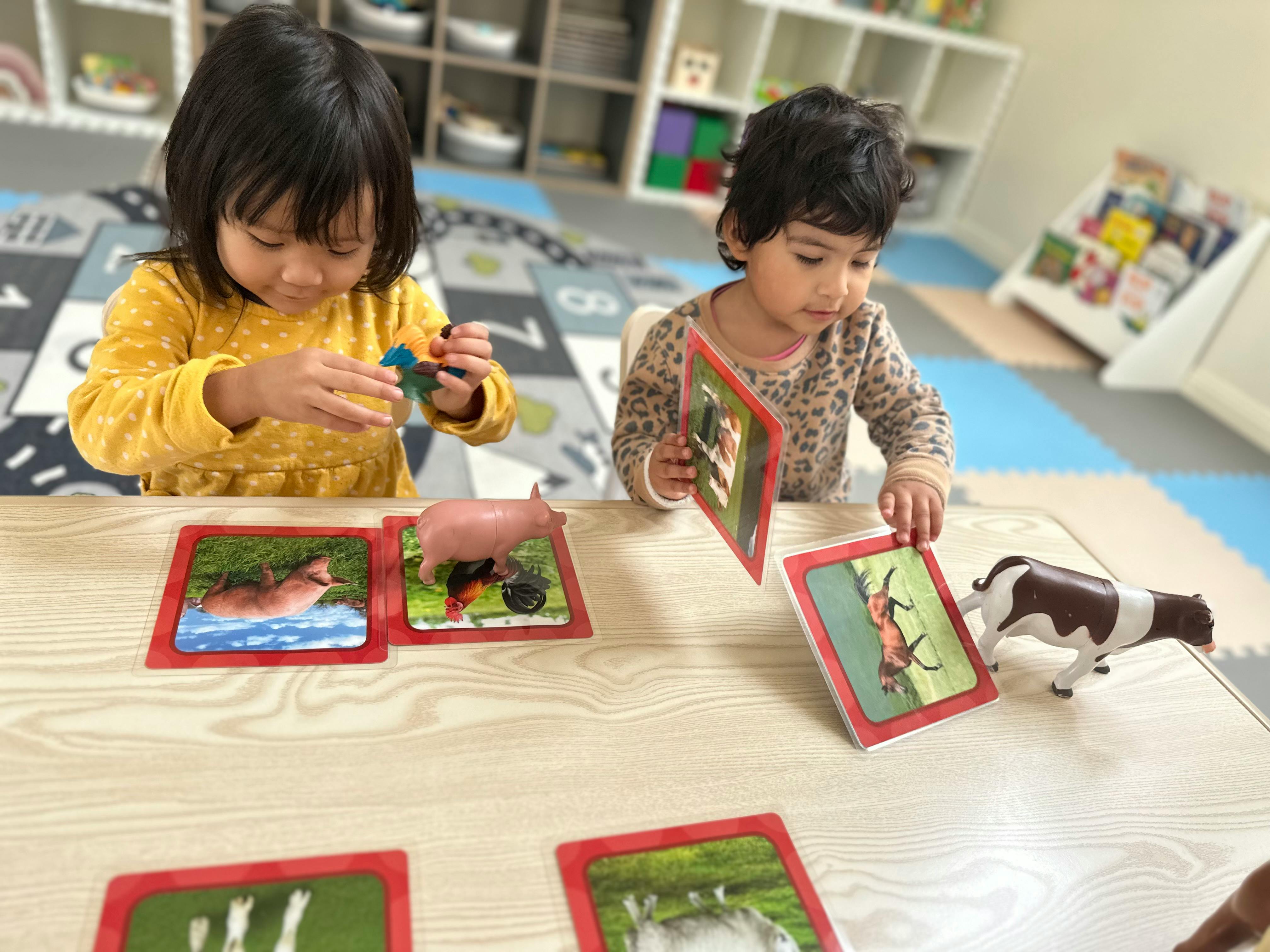 Two children playing with animal cards and figurines at a table