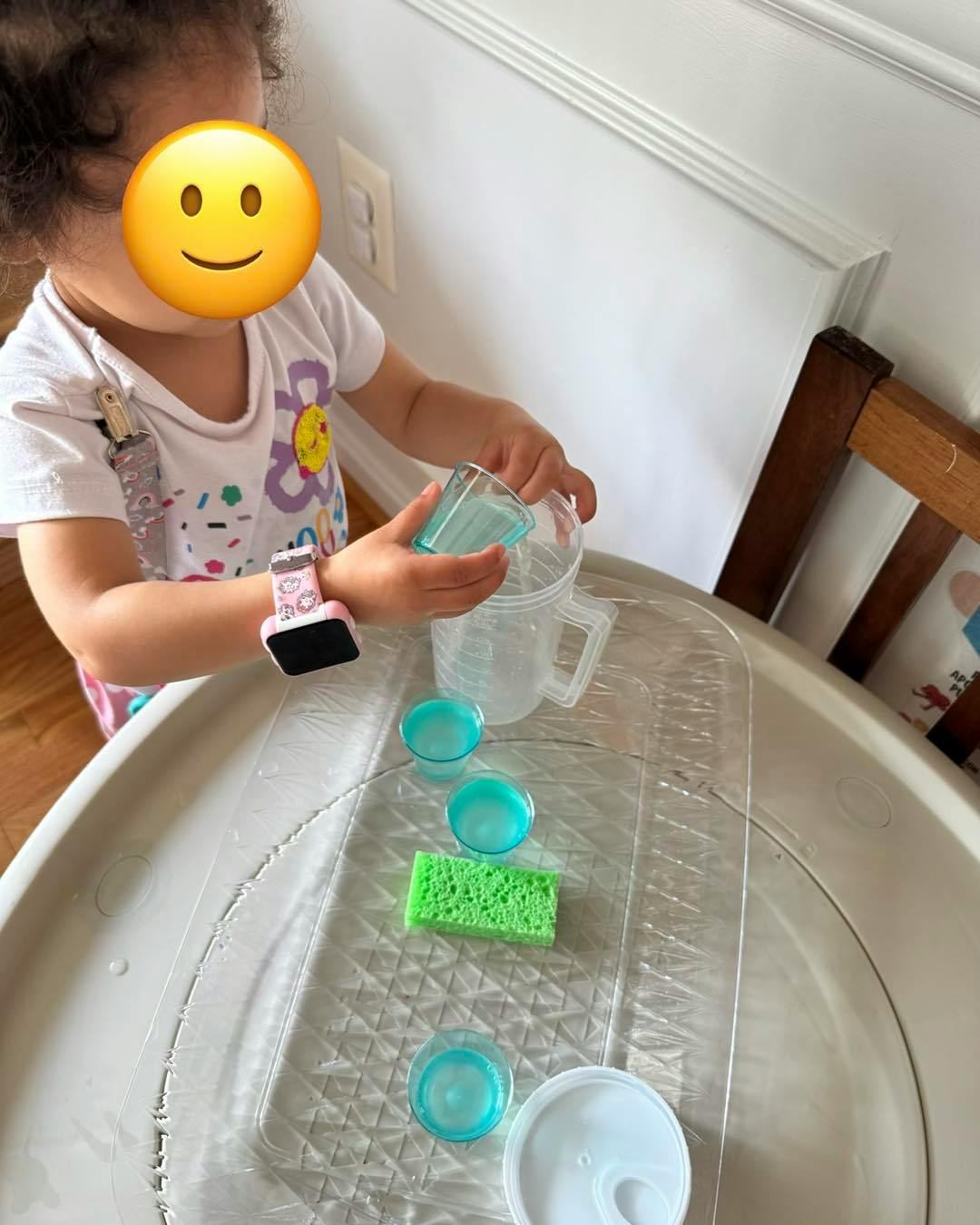 Child pouring water from a small cup into a measuring cup