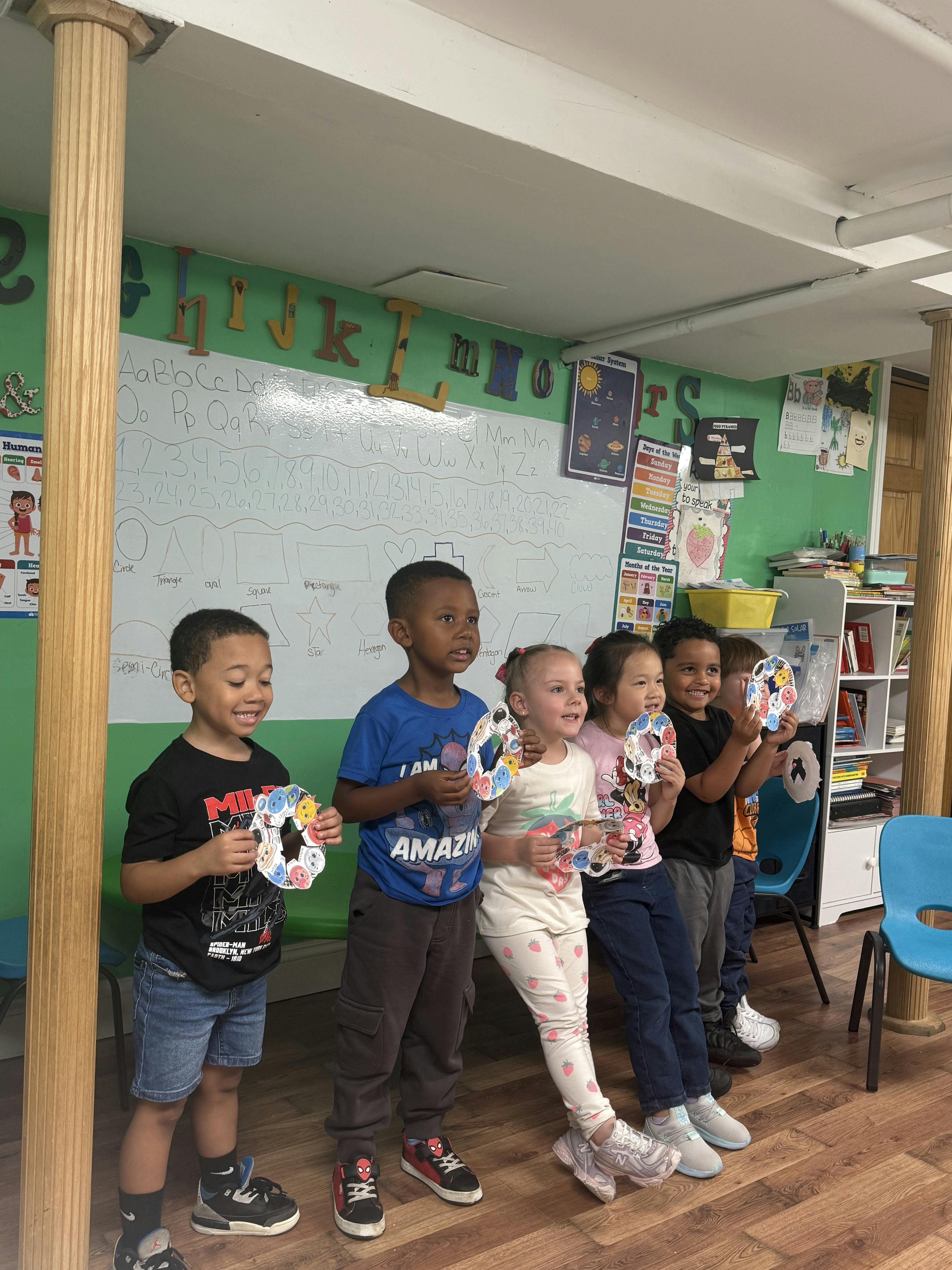 Group of children standing in a classroom holding craft projects