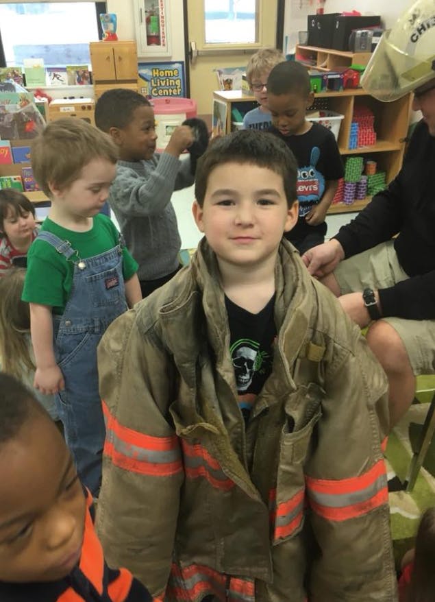 Child wearing an oversized firefighter jacket in a classroom