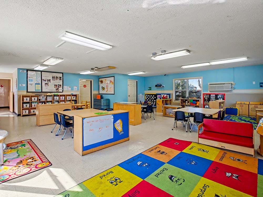 Classroom with child-sized tables, chairs, shelving, and colorful rugs