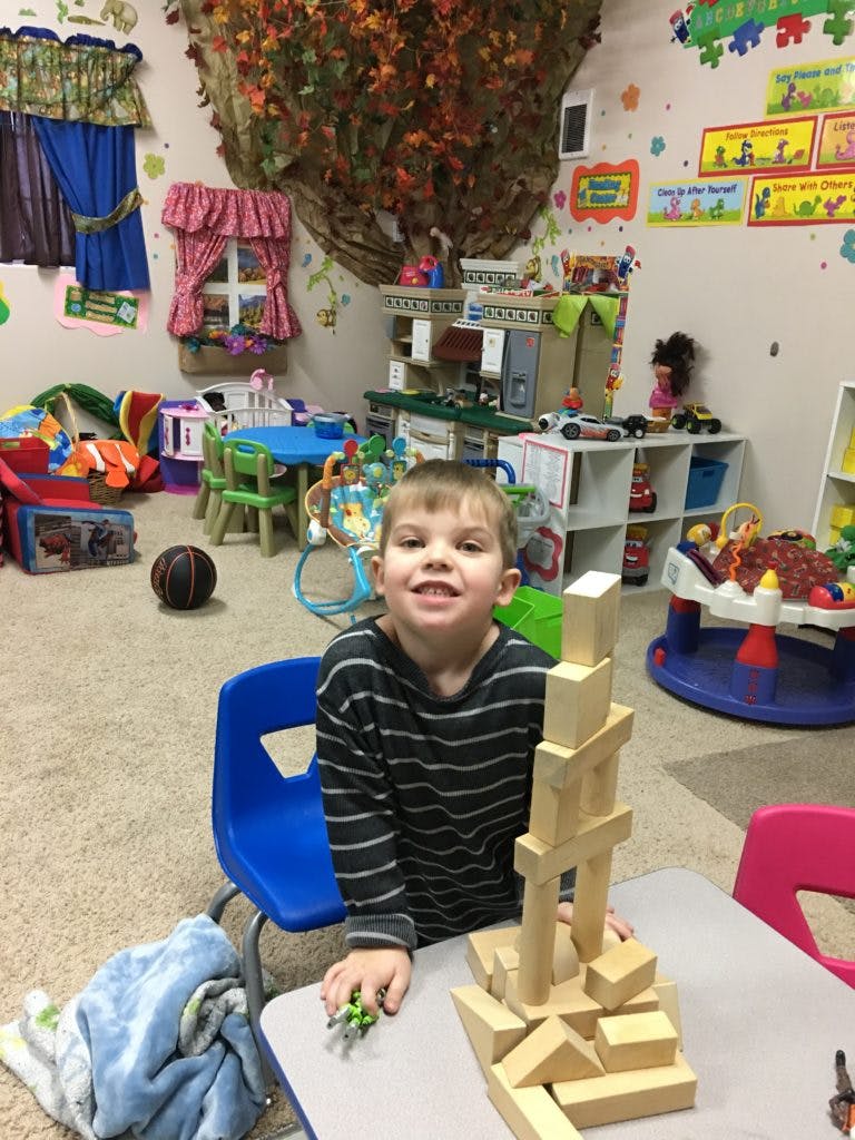 Child sitting at a table with a tall structure of wooden blocks