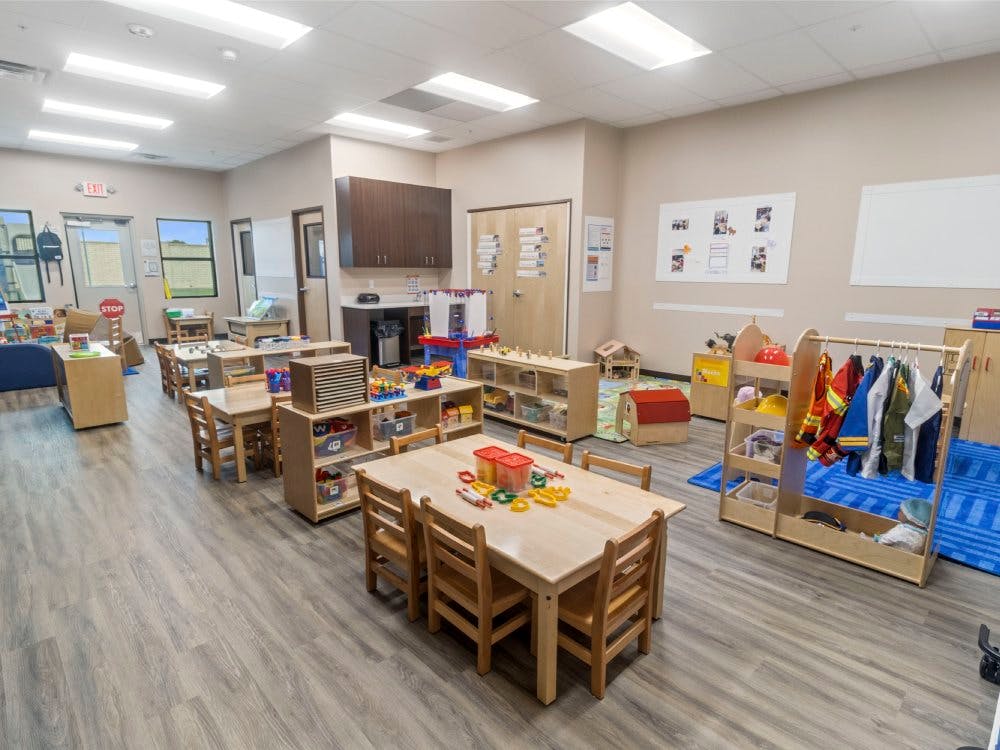 Empty classroom with small tables and chairs, toys, and dress-up clothes