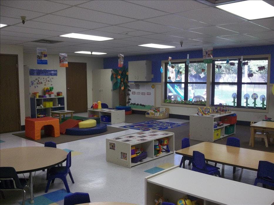 empty preschool classroom with tables, chairs, toys, and padded play structures