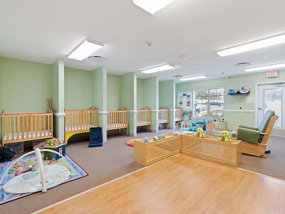 Cribs and play area in a brightly lit room with an "EXIT" sign above a door