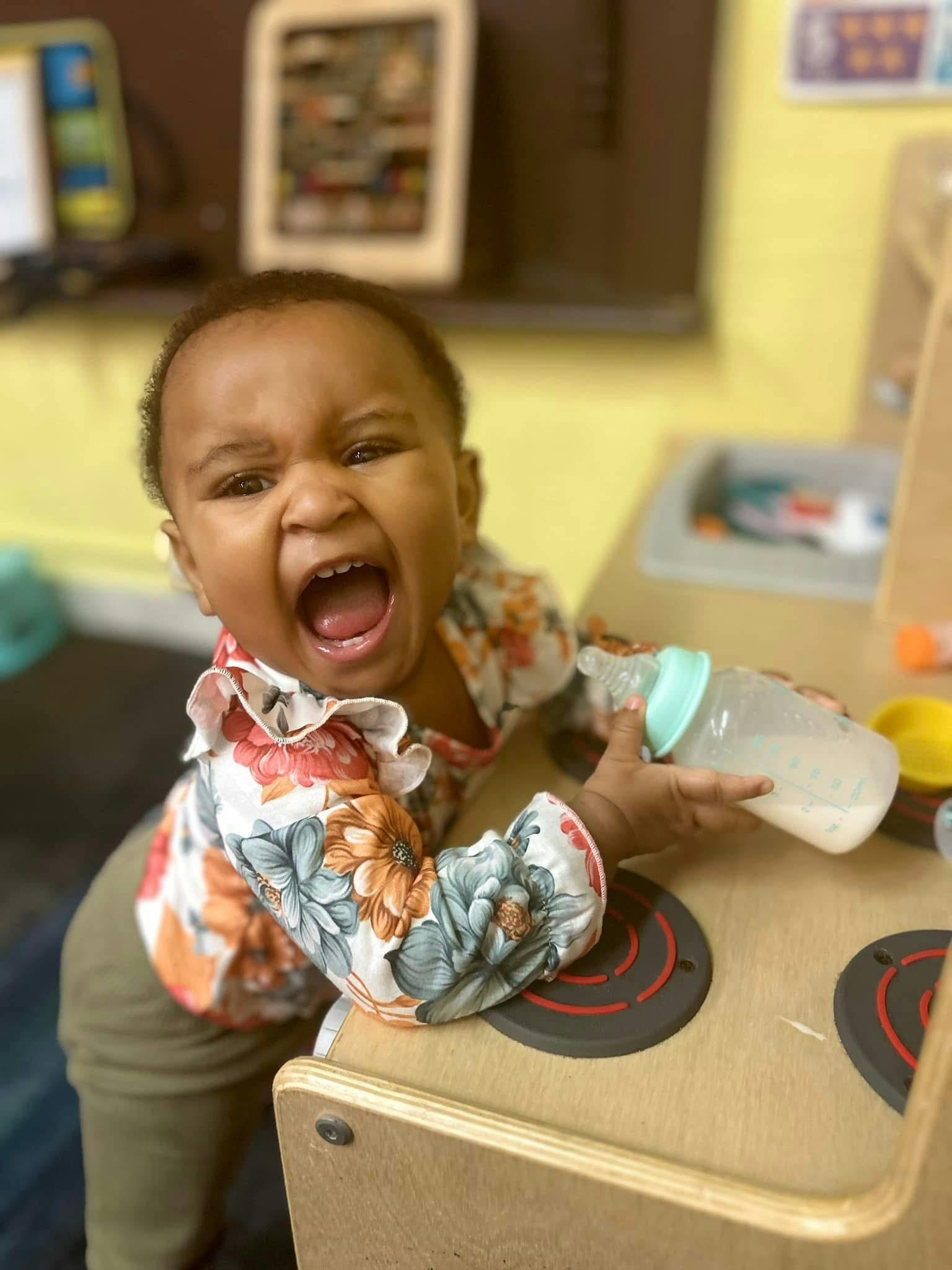 Child holding a baby bottle in a play kitchen