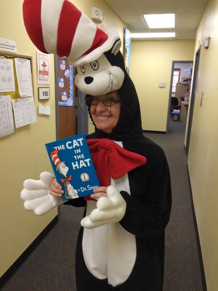Person in Cat in the Hat costume holding a book titled The Cat in the Hat