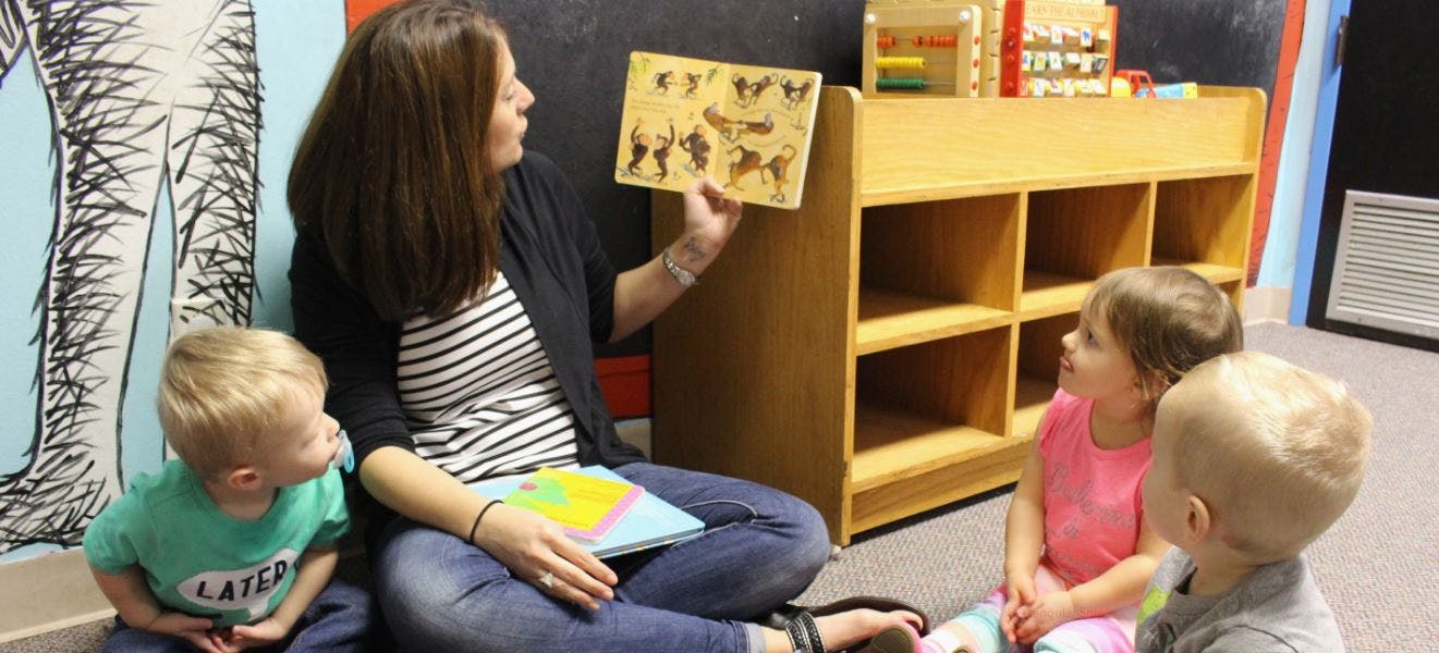 Person showing a book to three children in a classroom