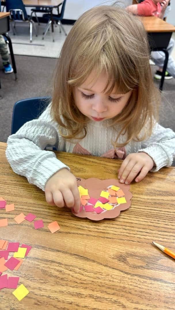 Child doing a craft with small paper squares at a desk