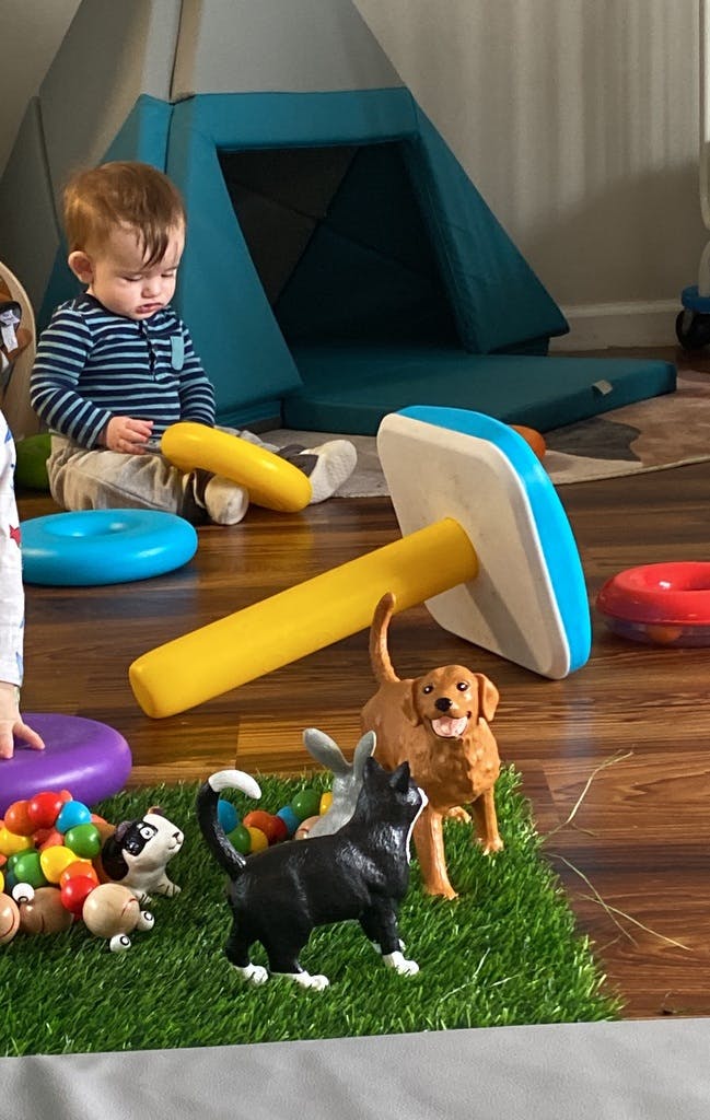 Child sitting on floor with toys, including a large yellow and blue toy hammer