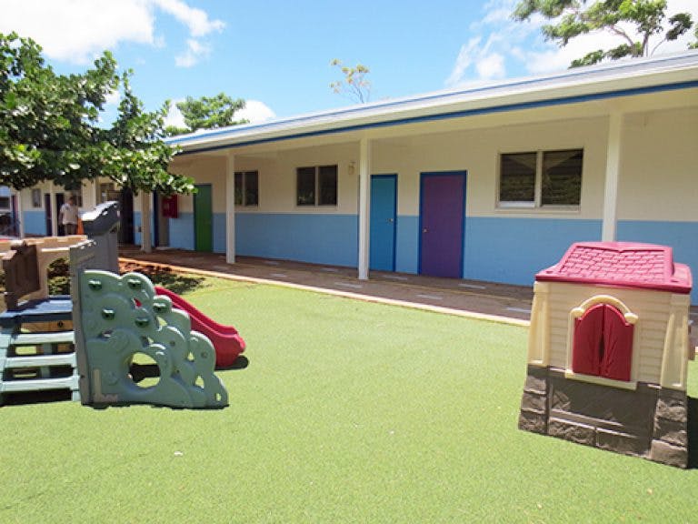 Playground with climbing structure, slide, and playhouse next to a building