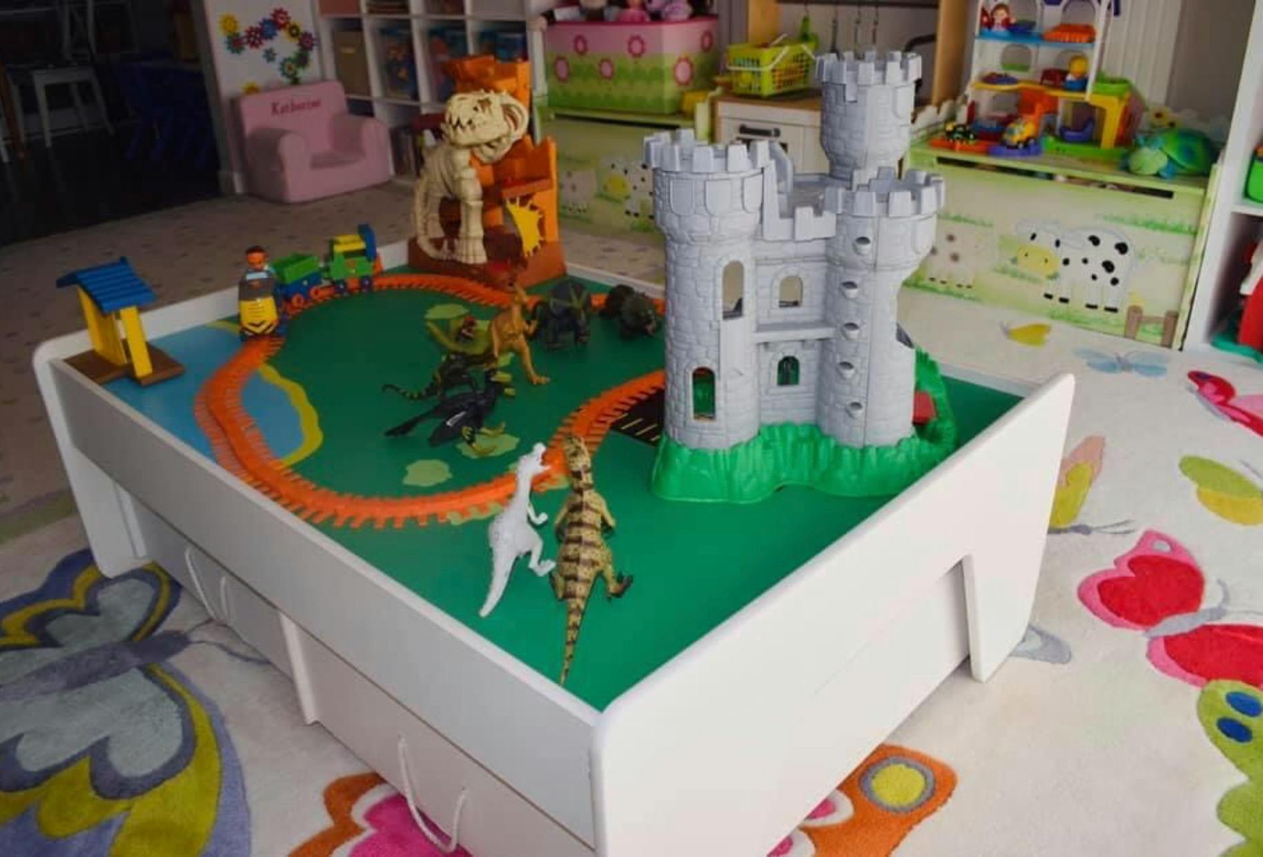 Play table with toy castle, dinosaurs, and train track