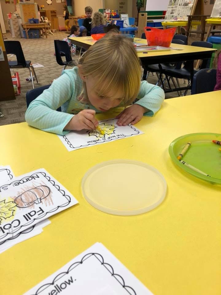 Child coloring a picture at a yellow table in a classroom