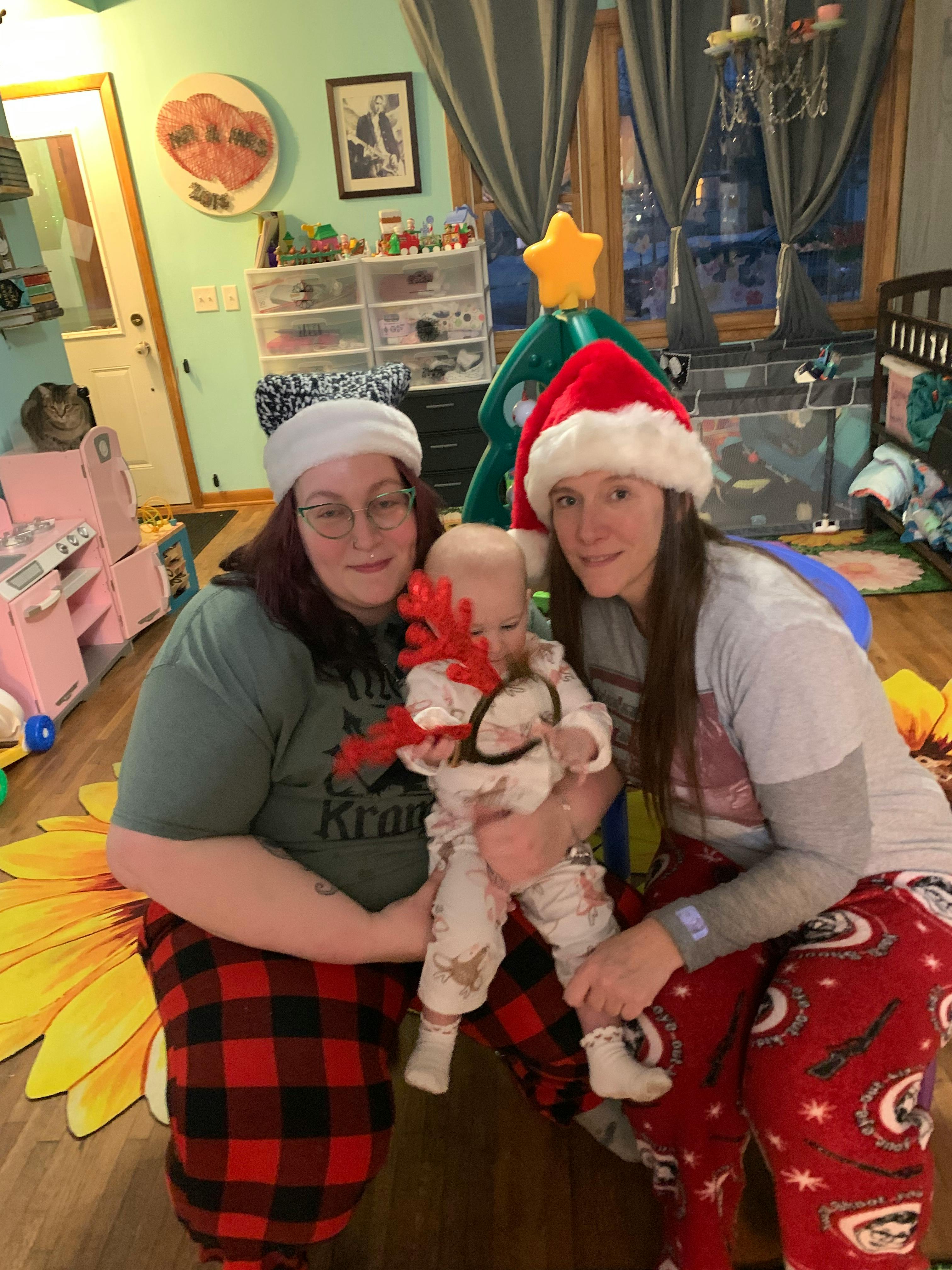 Two people in Santa hats holding a child wearing reindeer antlers