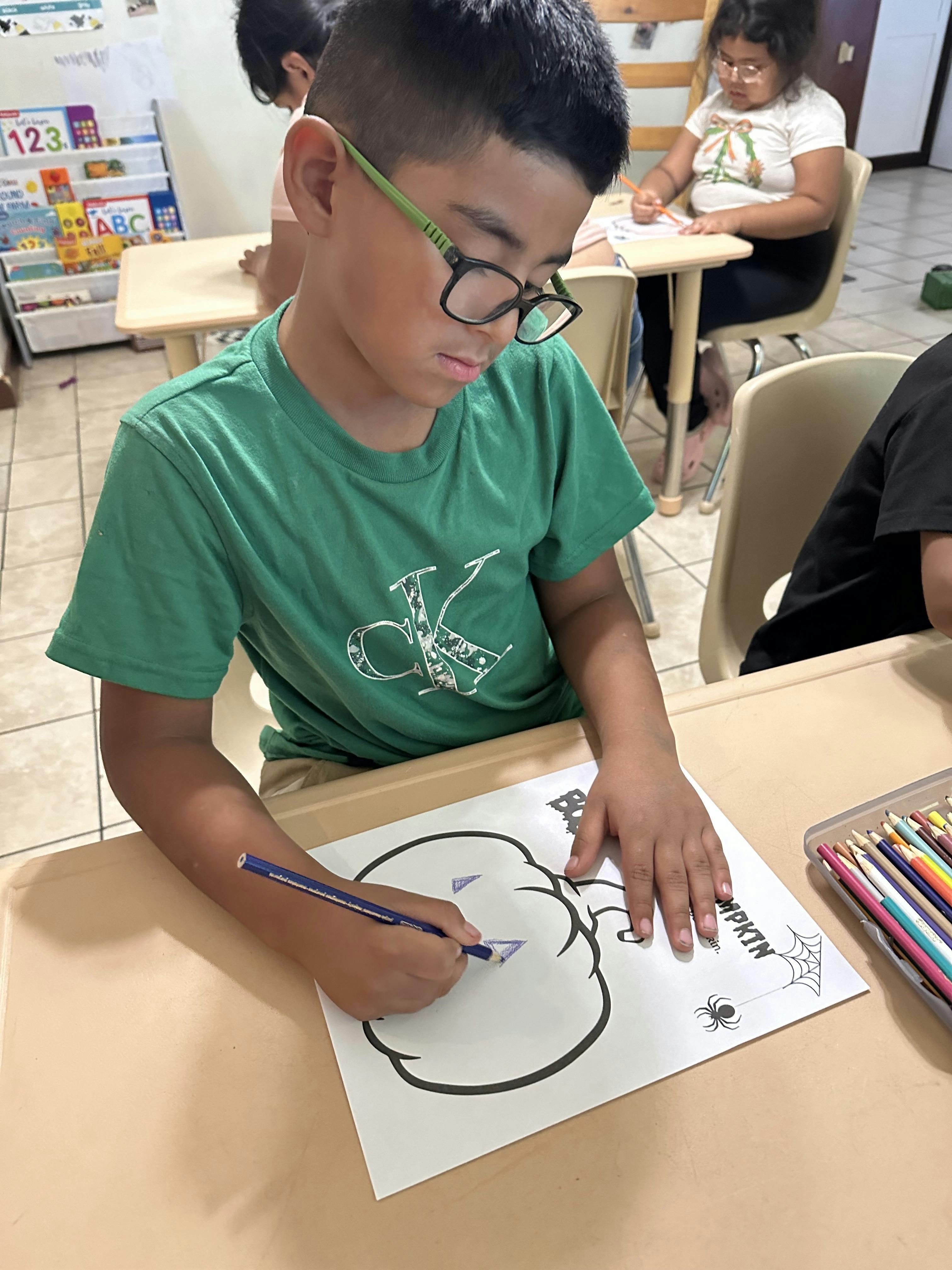 Child coloring a pumpkin drawing at a desk
