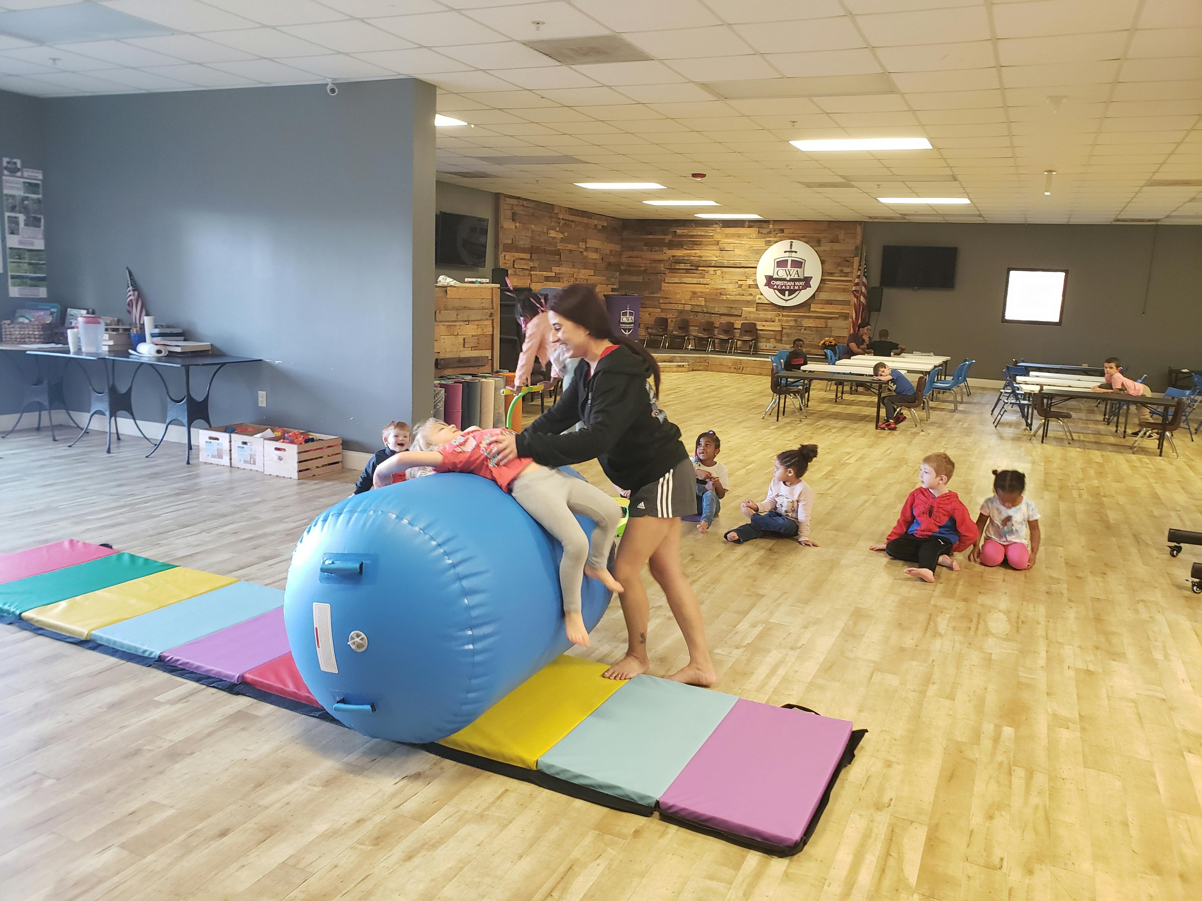 Person helping a child on a large blue inflatable roller in a gym