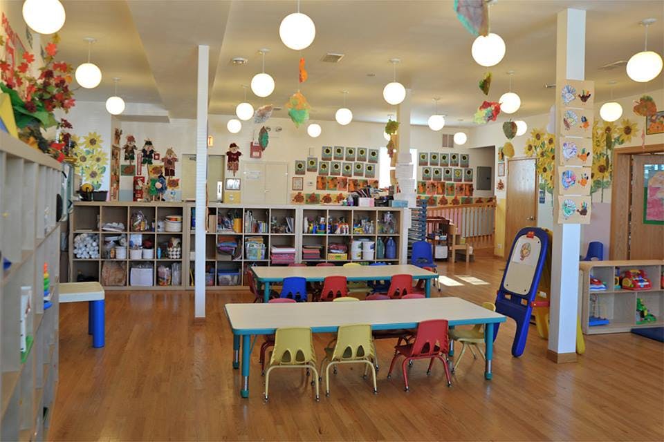 Classroom with small tables and chairs, shelves with supplies, and decorations