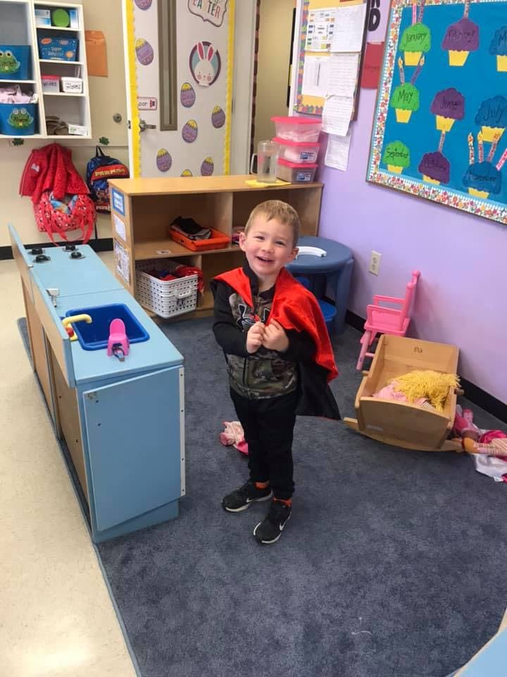 Child in a red cape standing in a classroom