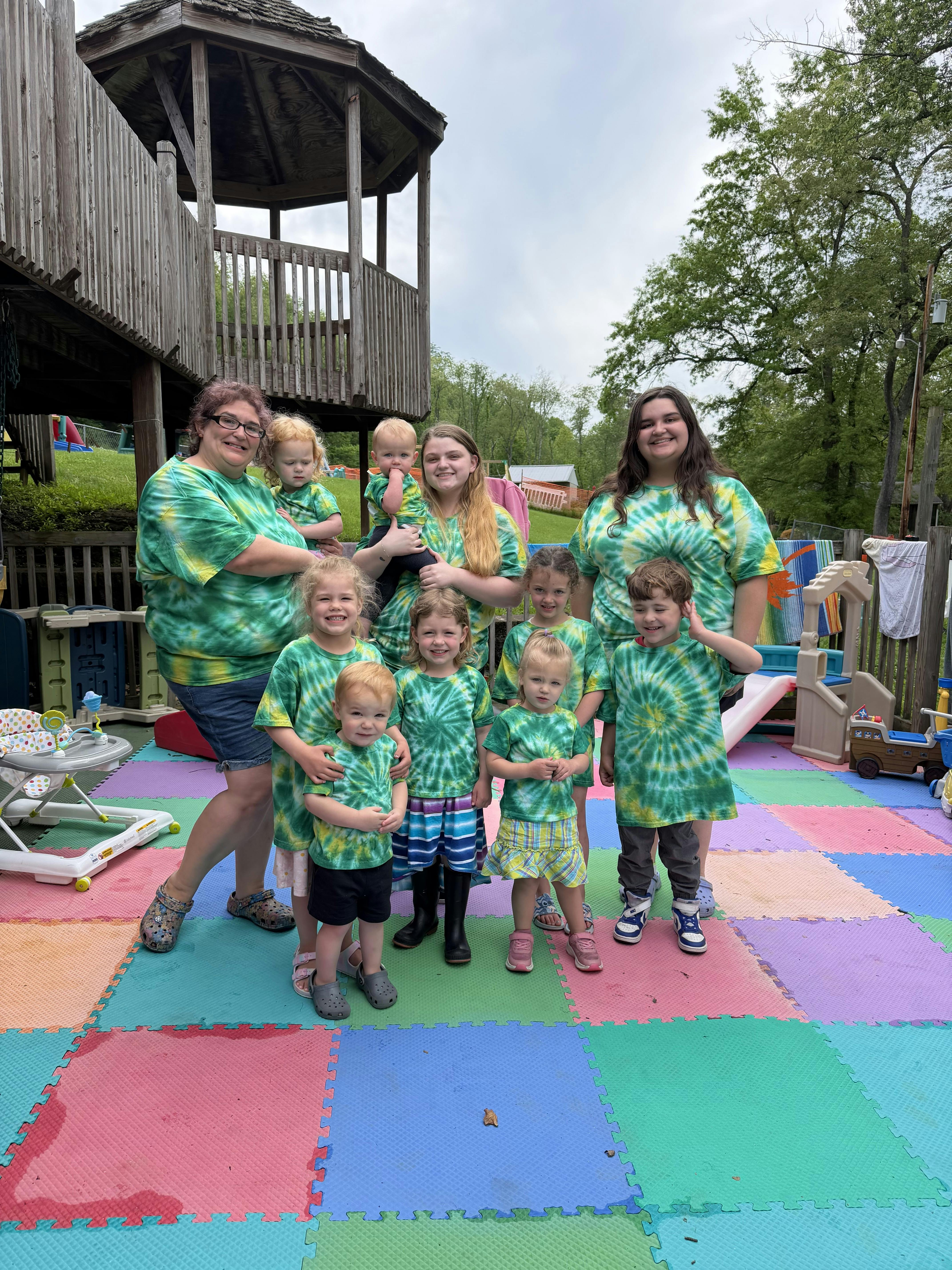 Group of people wearing matching tie-dye shirts on a colorful playground mat