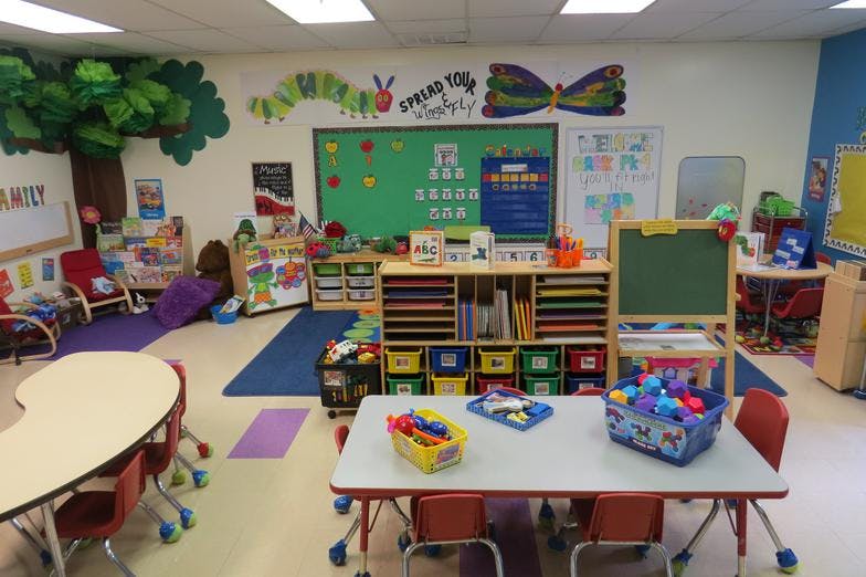 Classroom with small tables and chairs, storage shelves, and wall decorations