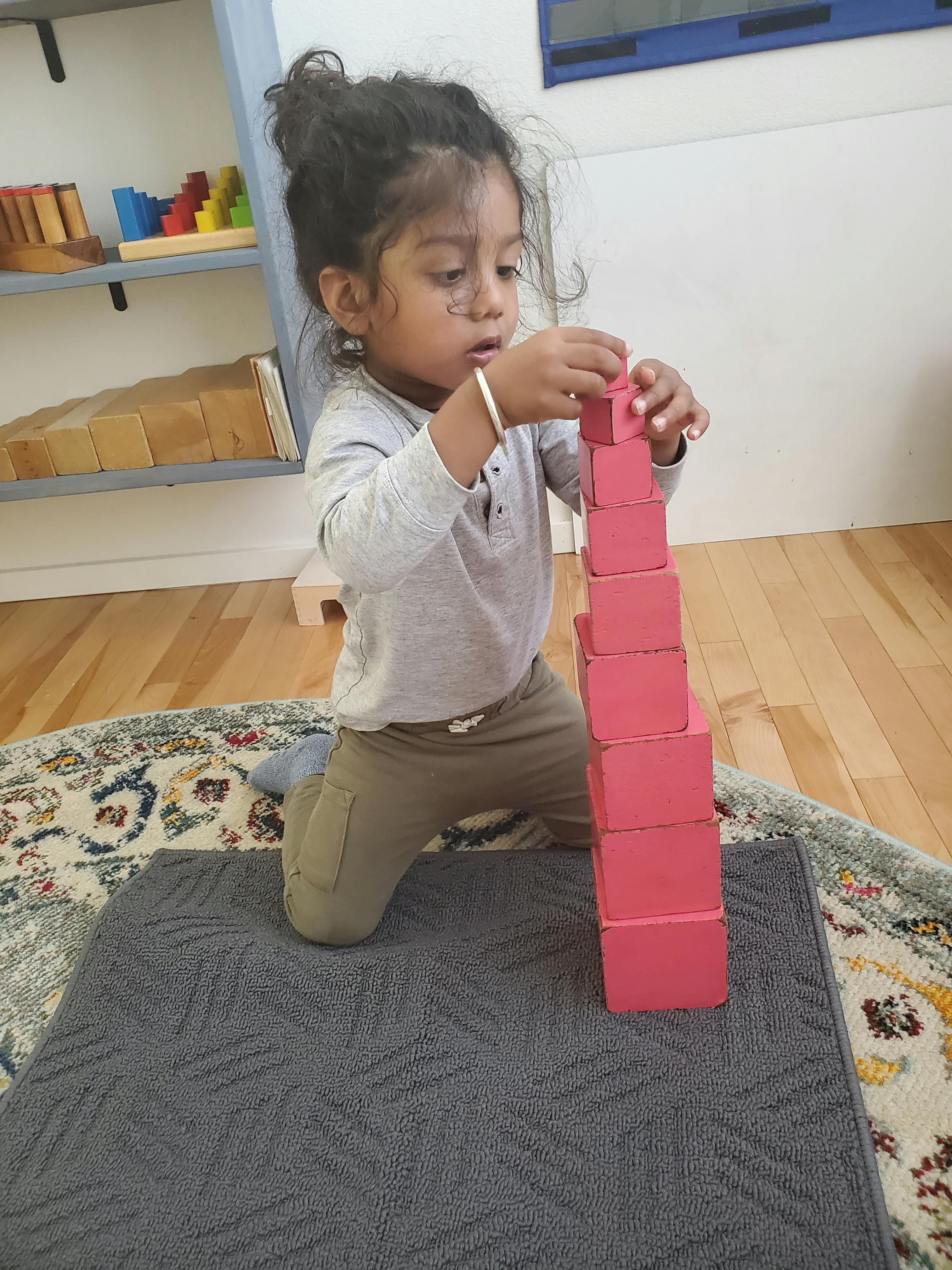 Child kneeling and stacking red blocks