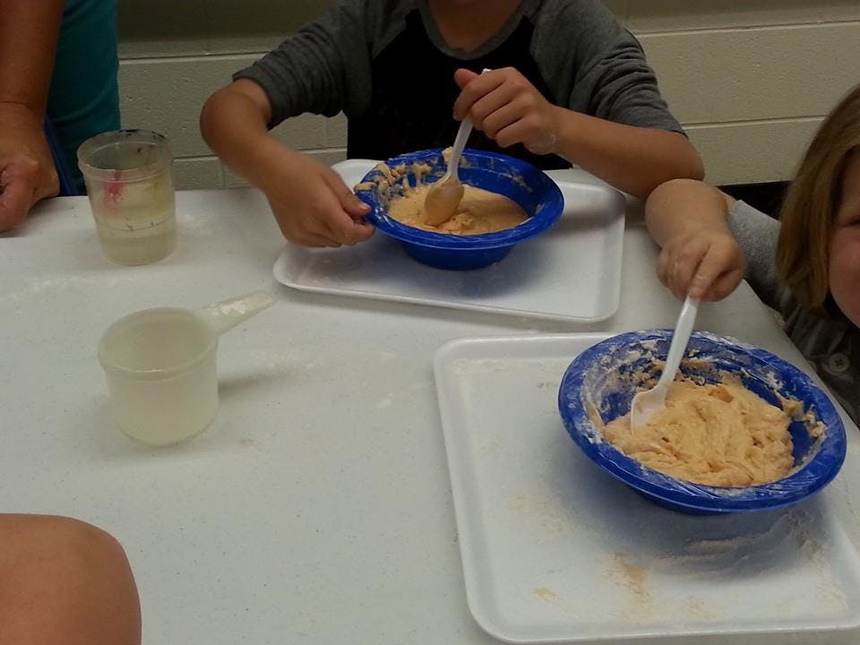 Two children mixing dough in blue bowls with spoons