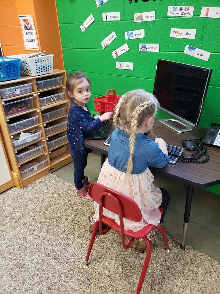 Two children at a computer desk in a classroom