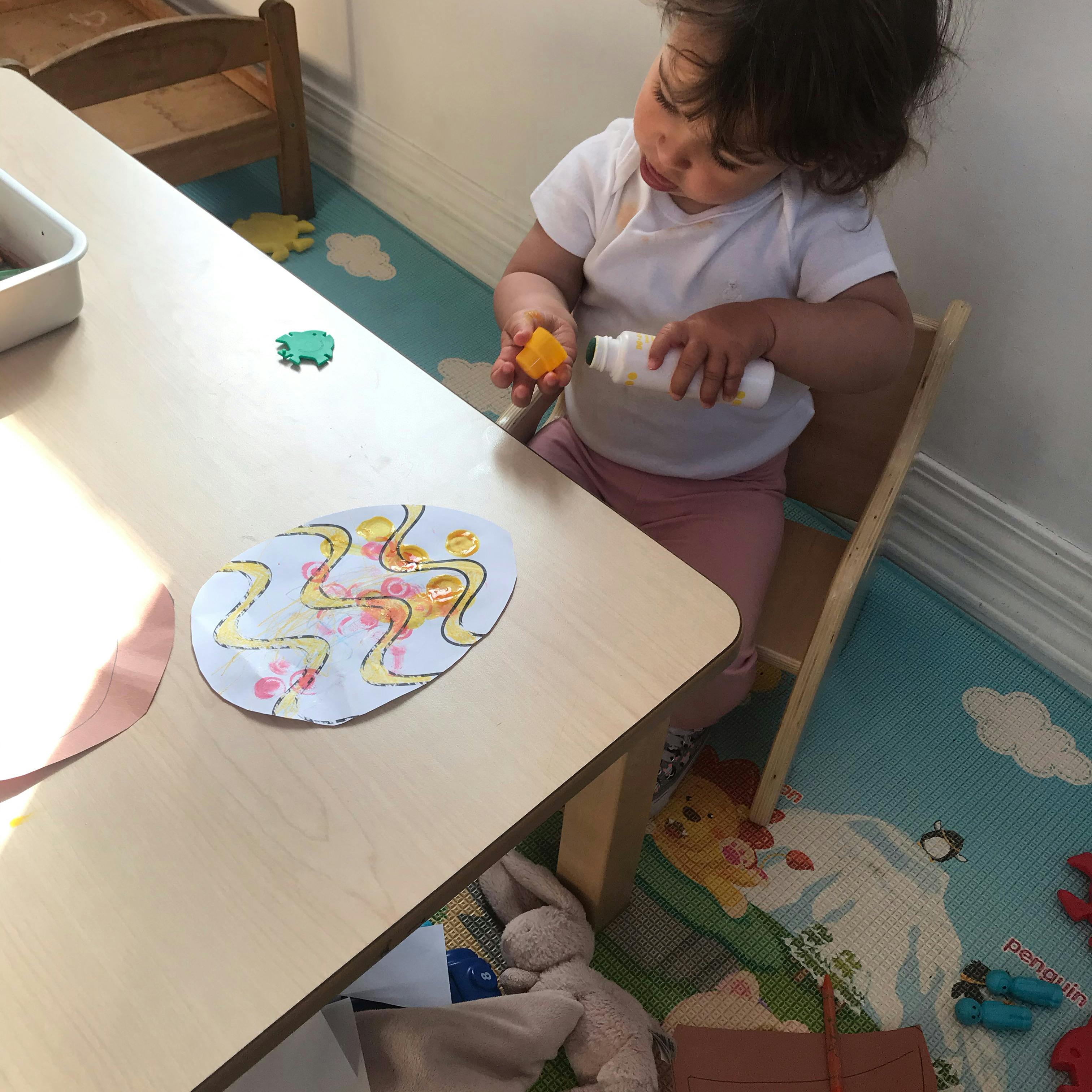 Child sitting at a table holding a bottle and a small object