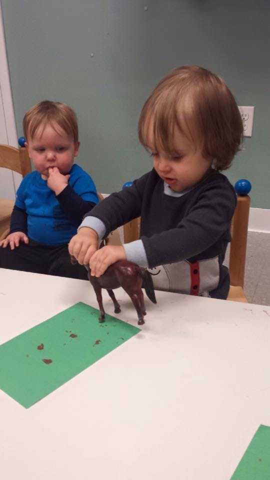 Child playing with a toy horse on a table, another child in the background
