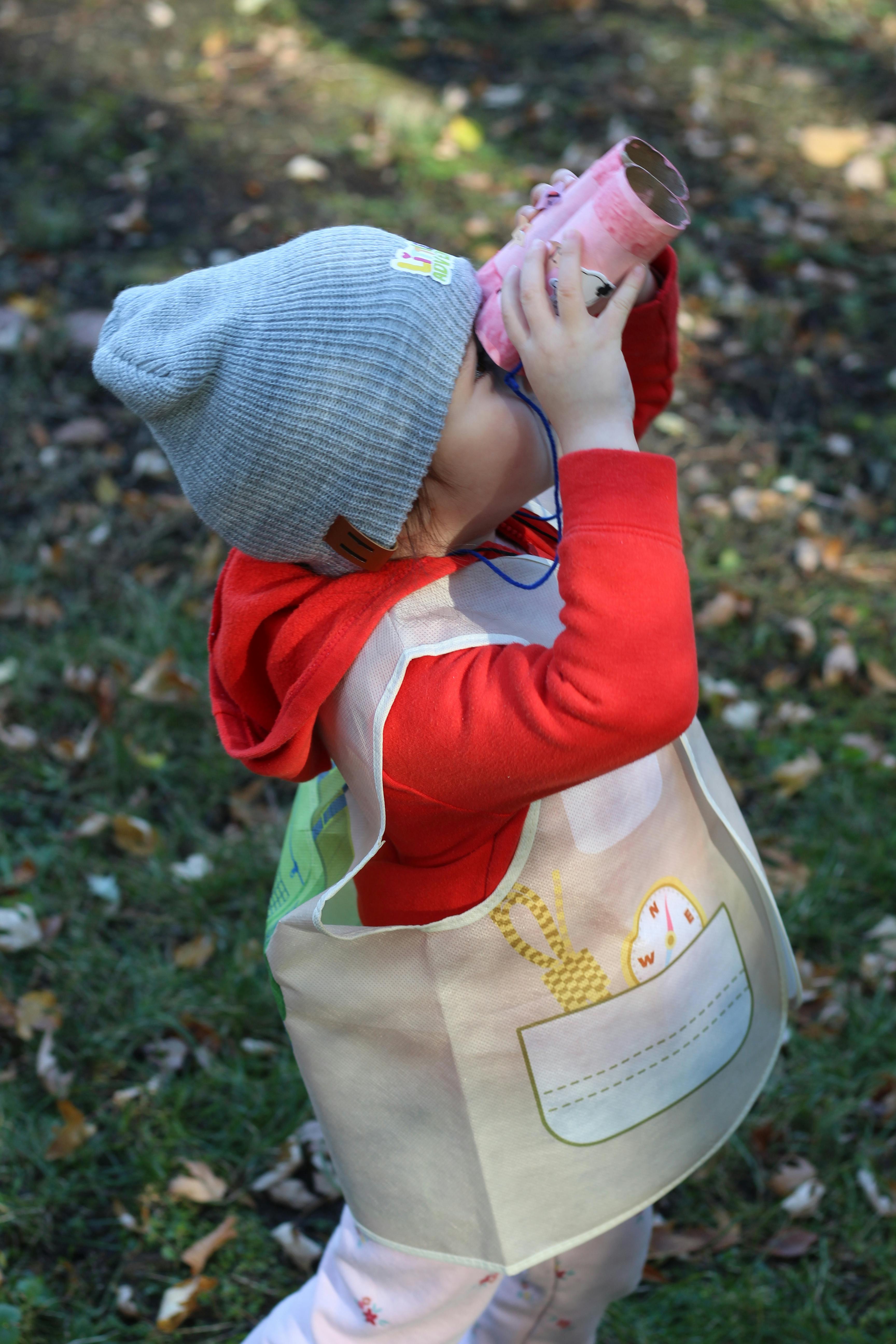 Child wearing a hat and red shirt looking through cardboard tube binoculars