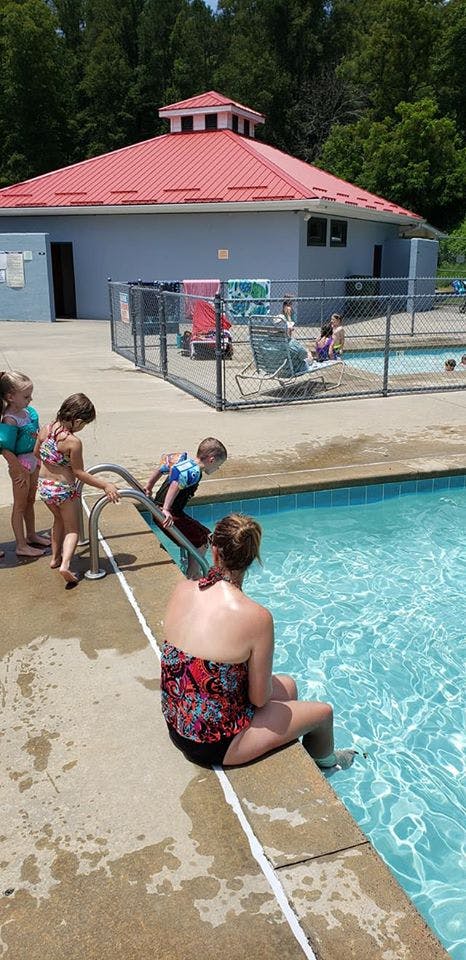 Person sitting at the edge of a pool with children entering the water