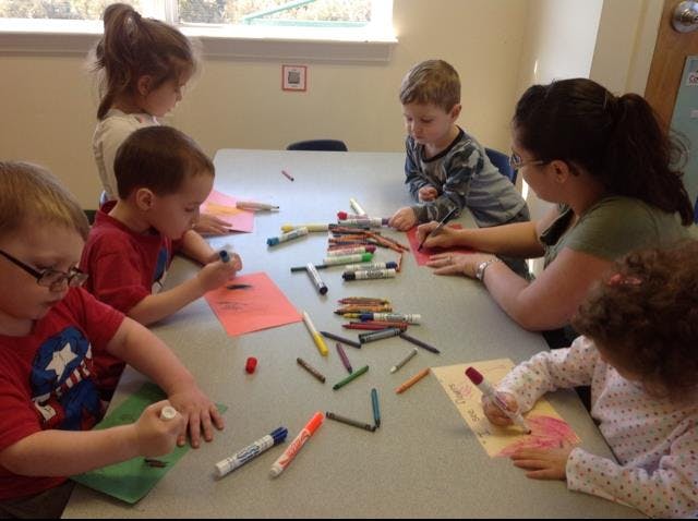 Adult and children drawing at a table with markers and crayons
