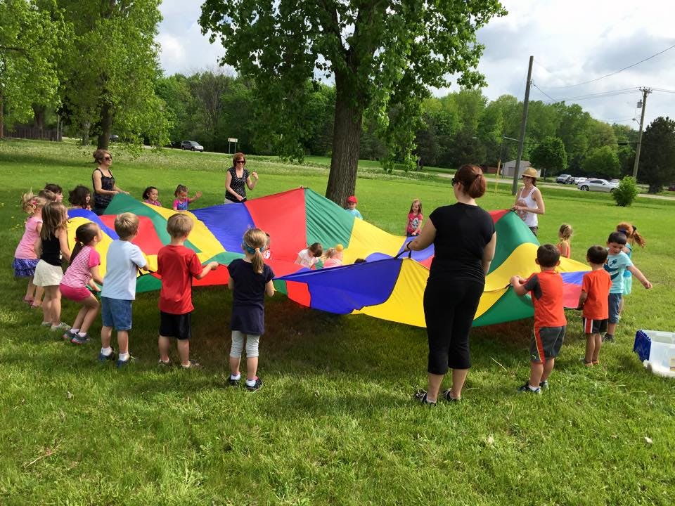 Adults and children playing with a colorful parachute on a grassy field