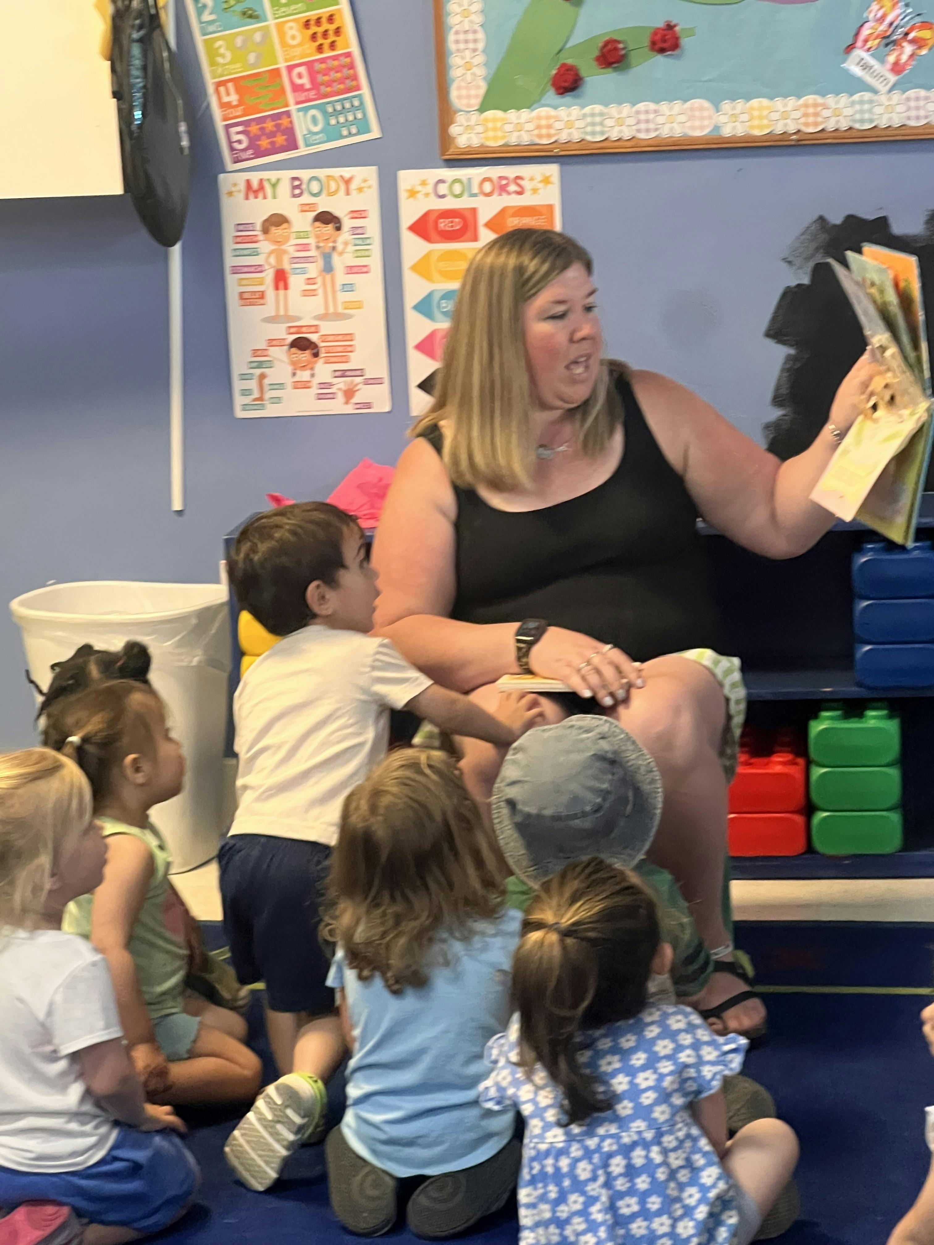 Adult reading a book to a group of children sitting on a classroom floor
