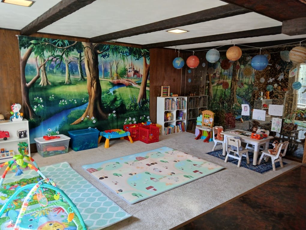 Playroom with forest mural, play mats, and small tables with chairs