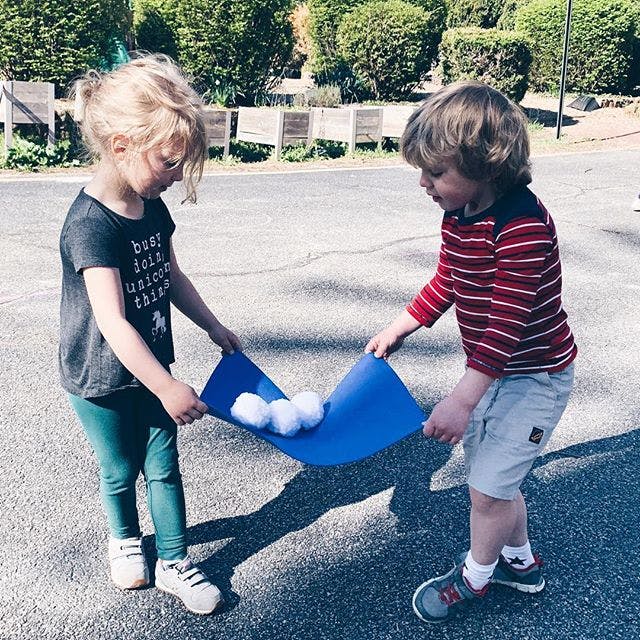 Two children holding a blue mat with white balls on it