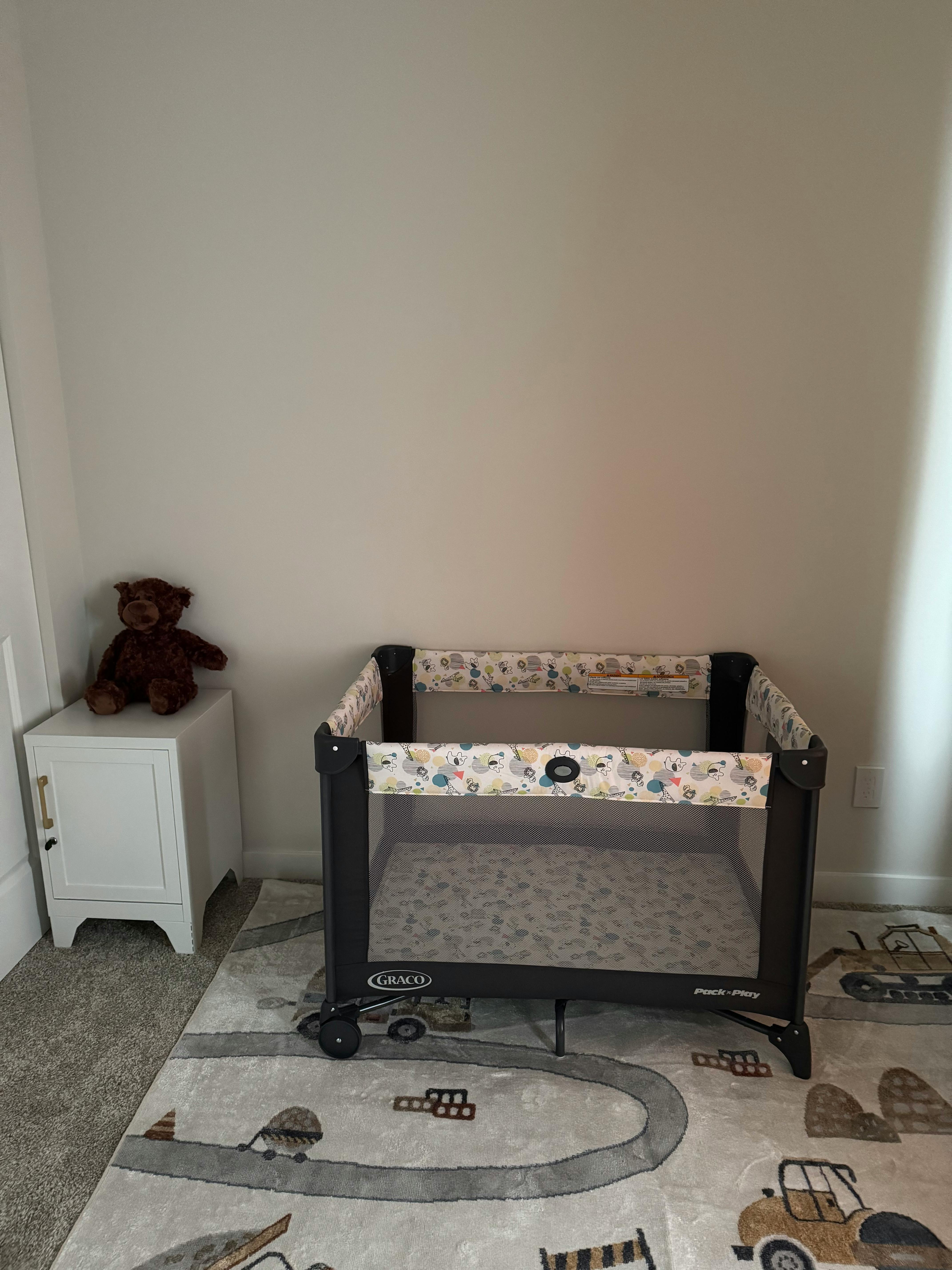 Playard with a teddy bear on a white cabinet next to it