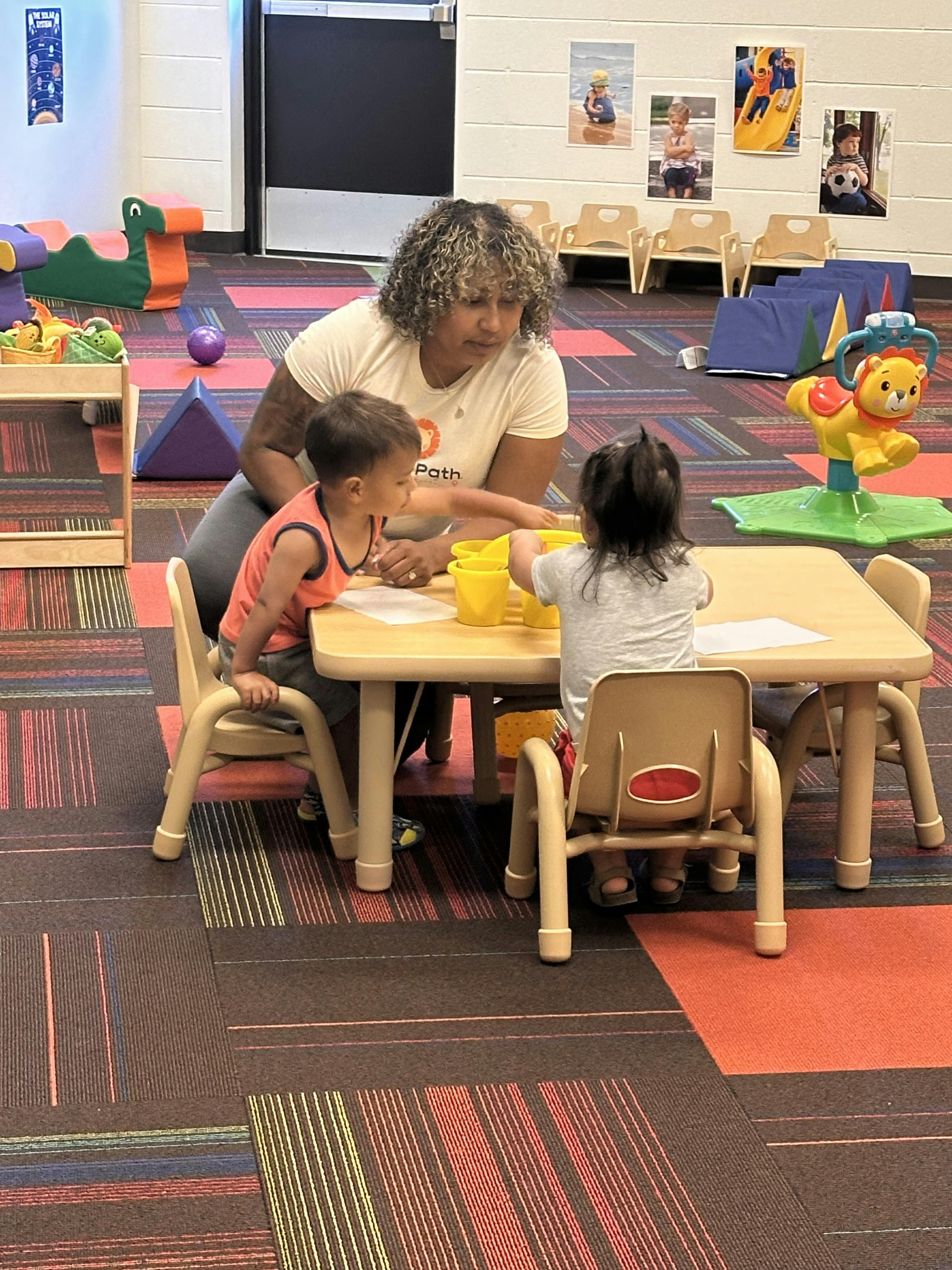 Adult and two children playing with yellow cups at a small table