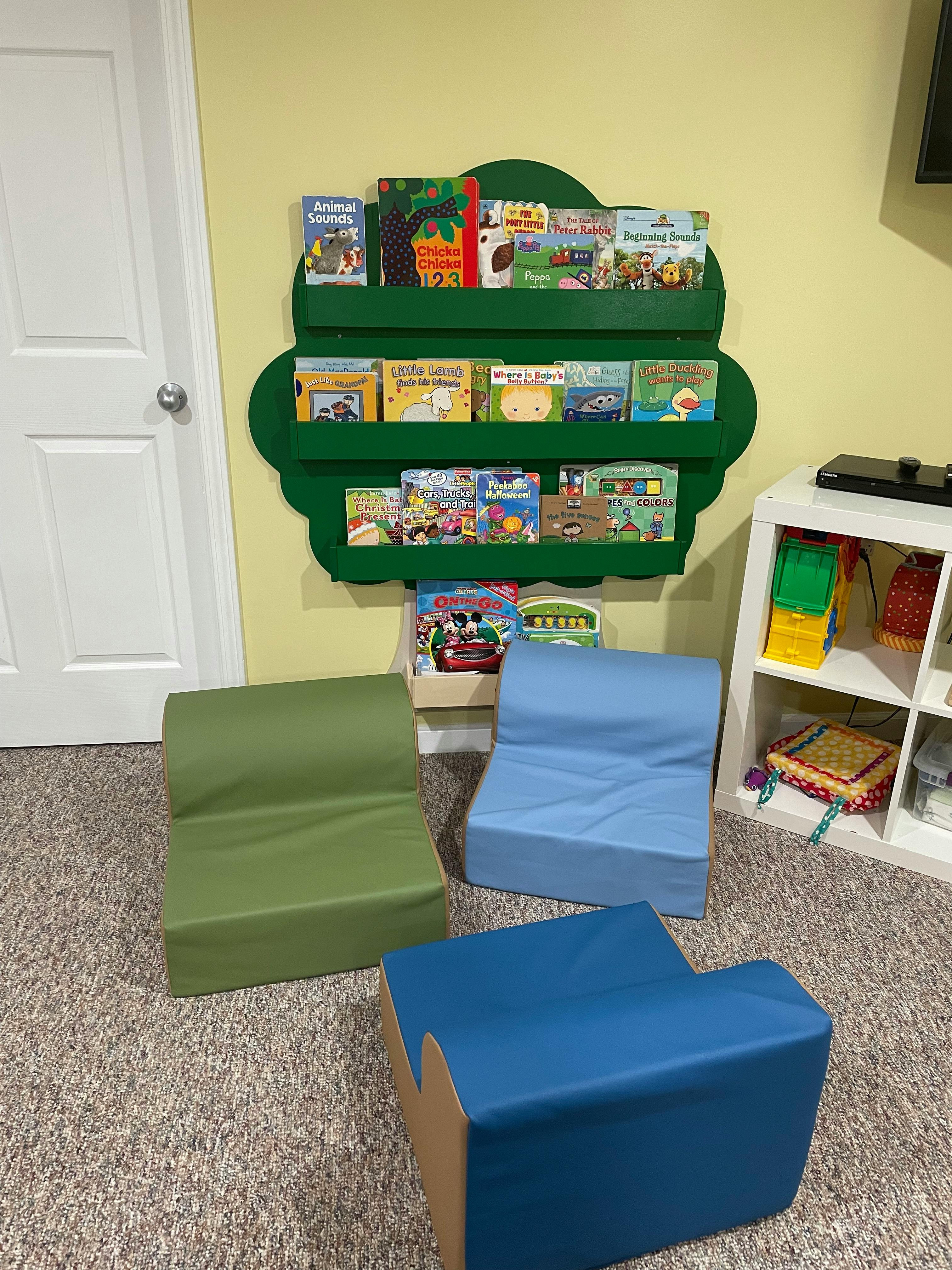 Green wall-mounted bookshelf with children's books and three floor chairs