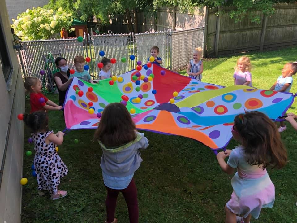 Children and an adult playing with a colorful parachute and small balls outdoors