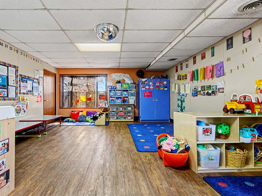 Empty classroom with colorful decorations, small tables, and shelves of toys