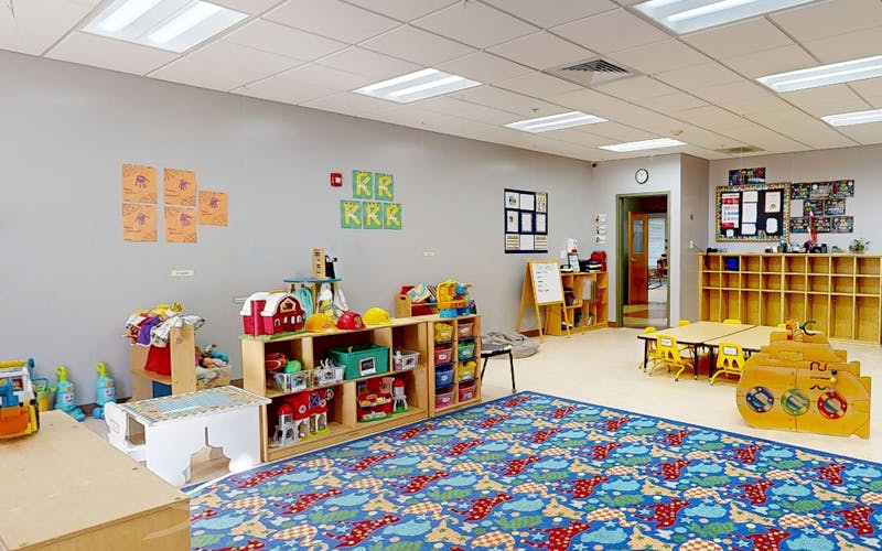 A classroom with toys, shelves, tables, and a colorful rug